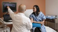 Physician points to ultrasound screen while patient watches.